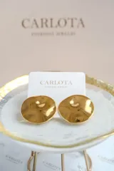 Caravanas circulares de diseño minimalista con superficie texturizada y acabado brillante. Presentan una forma ligeramente cóncava que refleja la luz, aportando un toque moderno y elegante.