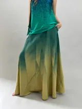 Falda larga de lana con diseño de paneles geométricos y efecto degradado que transiciona de verde esmeralda a tonos amarillentos. Presenta cintura alta, cierre invisible lateral y bolsillos ocultos.