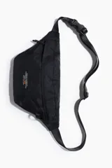 Cartera cruzada de nylon color negro, con cierre superior y bolsillo frontal con cierre. Incluye correa ajustable con hebilla plástica a presión y parche rectangular decorativo en el frente.