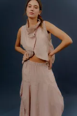Chaleco de lino color marfil o beige claro, con diseño sin mangas, cuello alto amplio, cierre frontal con botones y bolsillos delanteros amplios. Presenta un corte asimétrico y relajado.