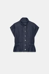 Chaleco de denim azul oscuro con cuello alto, manga sisa y cintura ajustable con elástico. Cierre frontal con botones a presión metálicos.
