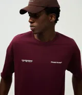 Remera de corte oversized color bordó, con cuello redondo y manga corta. Presenta un estampado en la espalda con lettering manuscrito que incluye las ciudades Paris, Tokyo y New York, junto con detalles tipográficos adicionales.