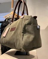 Bolso amplio de gamuza azul con manijas largas de cuero marrón. Cuenta con bolsillos laterales, uno con clip, cierre posterior y un bolsillo interno amplio. Presenta detalle de bandera y logo bordado en los laterales.