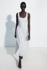 Vestido midi de corte corsetero color blanco, con escote redondo, tirantes finos y detalle de lazo en el delantero. Falda con frunces y cierre en la espalda con cremallera oculta.