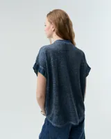 Remera blanca de lino con cuello mao, media cartera con broches metálicos y manga japonesa. Presenta un bolsillo frontal tipo plaqué, recortes laterales en sisa con detalles de encaje y ruedo redondeado con corte escalonado.