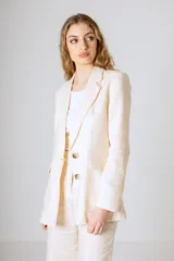 Blazer color beige confeccionado en lino, con solapas clásicas, cierre frontal de dos botones y bolsillos con solapa en los laterales.