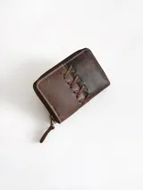 Billetera pequeña de cuero color chocolate con cierre perimetral metálico y detalle decorativo de cordones cruzados en el frente.