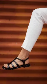 Sandalia plana tipo romana confeccionada 100% en cuero color negro, con múltiples tiras entrelazadas y cierre de hebilla lateral.