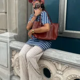 Bolso tipo tote amplio de cuero sintético en color marrón, con asas de hombro y detalles de costuras y hebillas decorativas.