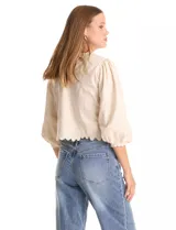 Blusa color beige con bordado floral al tono en el pecho y la espalda. Presenta mangas largas abullonadas con frunces en los hombros y puños festoneados. El ruedo cuenta con un acabado festoneado en ondas y la espalda incluye una abertura tipo gota con cierre de botón.