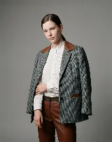 Blazer de paño de lana con diseño de pata de gallo en tonos gris y negro. Presenta cuello y detalles en los bolsillos de cuero color suela, con un corte relajado y cierre frontal de botones.