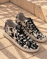 Zapatillas de cuero con estampado animal print tipo vaca en tonos blanco y negro, con cordones negros y suela de goma blanca.
