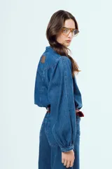 Camisa de denim azul oscuro con cuello mao, mangas abullonadas con puños elastizados y cierre frontal de botones metálicos.