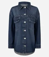Camisa de jean estilo overshirt con corte oversized, cuello clásico y mangas largas. Presenta cierre frontal con botones, dos bolsillos delanteros con solapa y aplicación de tachuelas metálicas en el cuello y la parte superior del pecho.