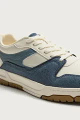 Zapatilla de básquet con cordones, diseño urbano de caña baja. Parte superior confeccionada en combinación de cuero sintético blanco y piezas de denim azul, con suela chunky de goma marrón y entresuela blanca.