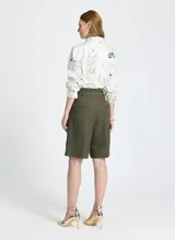 Bermuda verde oliva de lino, con corte entallado, cinturilla con trabillas, cierre de cremallera frontal con corchetes, pliegues delanteros, bolsillos de parche y un cordón a juego.