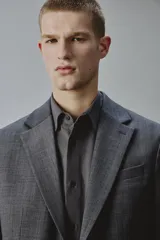 Blazer gris oscuro de corte regular fit con diseño de raya diplomática, confeccionado con mezcla de lana. Presenta solapas de muesca, cierre frontal de dos botones, bolsillos con solapa en la cadera y un bolsillo de vivo en el pecho.