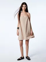 Vestido corto color beige, de breteles finos y escote recto. Cuenta con lazos laterales al costado del busto.