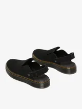 Zueco negro de gamuza con suela plana y correa ajustable en el talón.