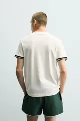 Camiseta de corte relajado confeccionada en piqué de algodón color crudo. Presenta cuello redondo, mangas cortas con ribetes a contraste y estampado frontal con el logo de Italia 90 FIFA World Cup.