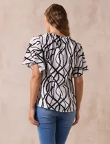 Blusa blanca estampada con líneas y lunares negros, de crepe marca Alex & Parker. Tiene cuello a la base, escote en V con botón y mangas cortas amplias.
