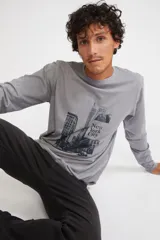 Remera de manga larga color gris melange, con cuello redondo y estampado gráfico en blanco y negro de la ciudad de Nueva York en el frente.