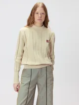 Sweater de punto color beige con cuello alto, detalles de paneles verticales texturizados y monograma bordado en el pecho.