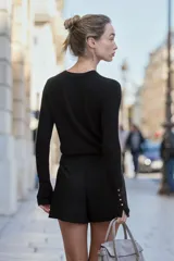 Jersey de punto liso con cuello redondo y manga larga. Presenta detalle de botones decorativos en los puños.