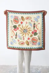 Pañuelo cuadrado de seda con estampado ilustrado de motivos veraniegos, incluyendo sol central, frutas, mariscos y elementos de picnic. Presenta un borde ancho en color marrón con detalles geométricos en verde y azul.