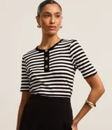 Blusa ajustada de mangas cortas, confeccionada en tejido de punto acanalado con rayas horizontales blancas y negras. Tiene cuello redondo con botones en la vista.