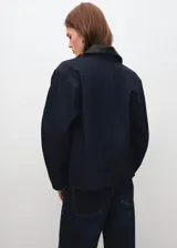 Chaqueta de denim en color azul oscuro, con diseño recto, cuello camisero, cierre frontal de botones metálicos y bolsillos de parche con solapa en el pecho.
