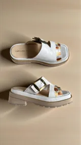 Sandalias de cuero natural blanco modelo Rina, con leve plataforma y suela dentada. Presentan una tira ancha cruzada con detalle pintado a mano multicolor y una hebilla metálica personalizada en tono oro viejo.