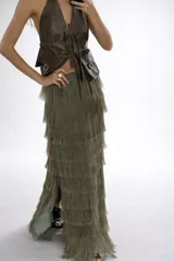 Falda larga color verde oliva, confeccionada en lino con capas de flecos de rafia que cubren toda la prenda. Presenta tajos laterales y cintura elástica en la parte posterior.
