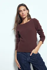 Remera de manga larga con ajuste al cuerpo, confeccionada en tejido acanalado de color marrón. Presenta cuello redondo y terminaciones con borde ondulado en puños y ruedo.