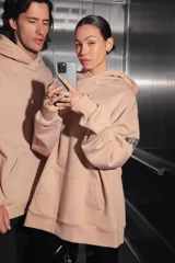 Buzo oversize color nude confeccionado en frisa, con capucha amplia, bolsillo canguro, terminaciones de puño y ruedo con rib, y logo de la marca bordado en el centro delantero.