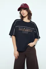 Remera negra de manga corta con estampado tipográfico "City of Angels California 1997" en tonos marrones y costuras visibles en blanco.