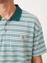 Chomba Rusty modelo Baviera de corte holgado, con diseño a rayas horizontales en tonos azul y beige. Cuenta con cuello mao, cierre frontal con botones y parche bordado con logo en el pecho.