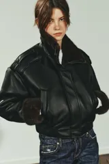 Cazadora bomber de efecto piel en color negro, con cuello subido, manga larga y bajo elástico. Presenta interior y puños con aplicación de pelo sintético en color marrón a contraste, cierre frontal con cremallera y botones a presión, y bolsillos laterales de vivo.