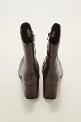 Bota corta de caña media en color negro, confeccionada en eco cuero con acabado brillante. Presenta cierre lateral interno, costura central decorativa en el empeine y taco cuadrado de altura media.