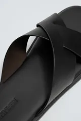 Sandalia plana de cuero negro con dos tiras anchas cruzadas en el empeine y plantilla anatómica.