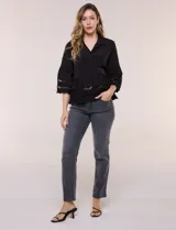Camisa negra de poliéster con cuello camisero, escote en V y cierre frontal de botones. Cuenta con mangas anchas de corte acampanado y detalles de bordado suizo calado en las mangas y en el ruedo inferior.