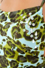 Traje de baño enterizo con estampado animal print en tonos verde y celeste. Presenta breteles finos, incrustaciones de tachas metálicas en la parte superior y jaretas laterales ajustables.