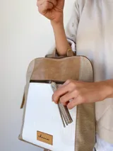 Mochila de diseño tricolor con paneles en beige, blanco con textura tipo reptil y detalles en cuero sintético marrón. Cuenta con un bolsillo frontal con cierre, correas ajustables y etiqueta de marca en la parte inferior.
