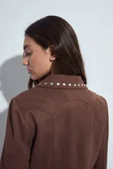 Campera estilo biker de símil gamuza color marrón, con cierre frontal y detalles de tachas metálicas en solapas, mangas y ruedo.