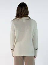 Sweater de punto azul marino con cuello en V, mangas largas con puños acanalados y detalle de línea en color marrón en el cuello y puños. Presenta un pequeño aplique decorativo en la parte inferior.