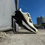 Championes Nike Air Max 90 con diseño clásico, combinando paneles de cuero blanco, beige y detalles en negro con textura de reptil. Cuenta con la icónica unidad de aire visible en el talón y suela de goma resistente.