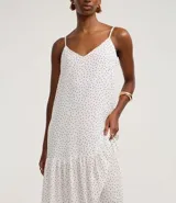 Vestido largo de corte evasé confeccionado en crepé, con escote en V, breteles finos ajustables y detalle de ruedo fruncido. Presenta una estampa clásica de lunares.