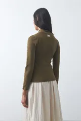 Polera de tejido de punto color celeste, con cuello alto y textura de pequeños puntos en relieve formando una cuadrícula en el frente y las mangas. De corte ajustado y manga larga.