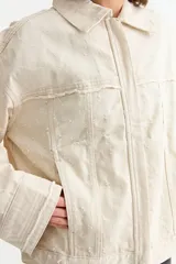 Campera de jean color crudo con diseño de corte holgado, cuello clásico, cierre frontal y detalles de desgastes en toda la prenda.