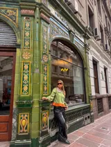 Camisa de manga larga en color verde oliva, con cuello babero en tono contrastante y detalle de volado en el ruedo en color naranja. Presenta cierre frontal con botones y mangas abullonadas con puños ajustados.